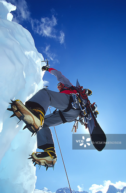 一个登山运动员用他的滑雪板在冰上爬下来。图片素材