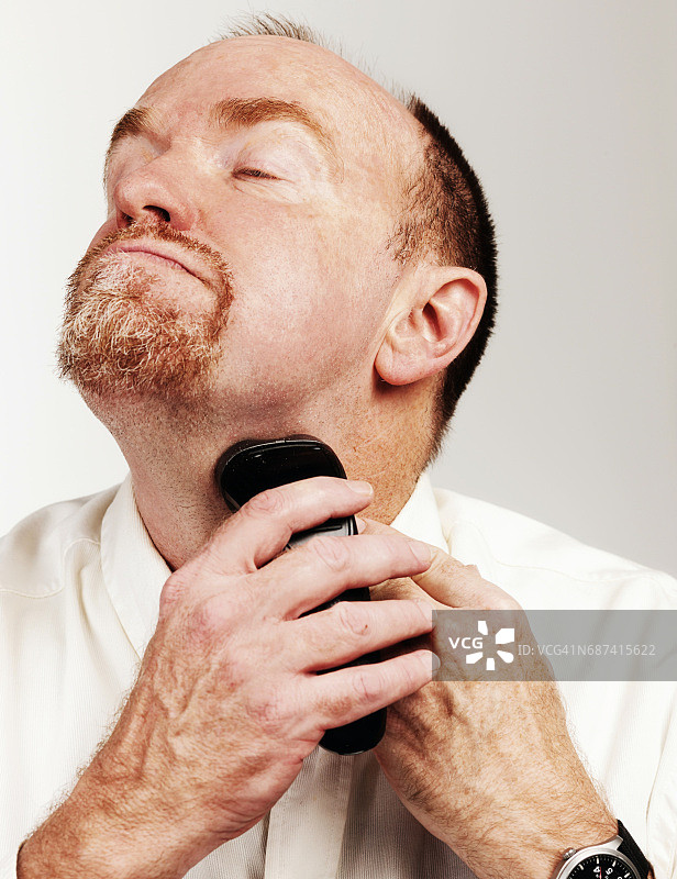 大胡子男子用电动剃须刀浓缩剃须，伸长脖子图片素材