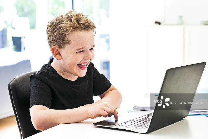 男孩笑着在家里的笔记本电脑上打字图片素材