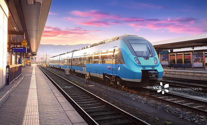 美丽的风景与现代的通勤列车在火车站和彩色天空与云彩日落在欧洲。蓝色火车站台的工业景观。铁路的背景图片素材