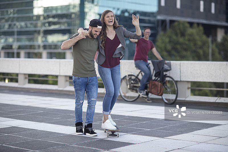 年轻男子扶着在滑板上笑着的女友图片素材
