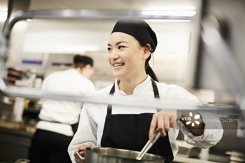 微笑女厨师在餐厅厨房搅拌锅图片素材