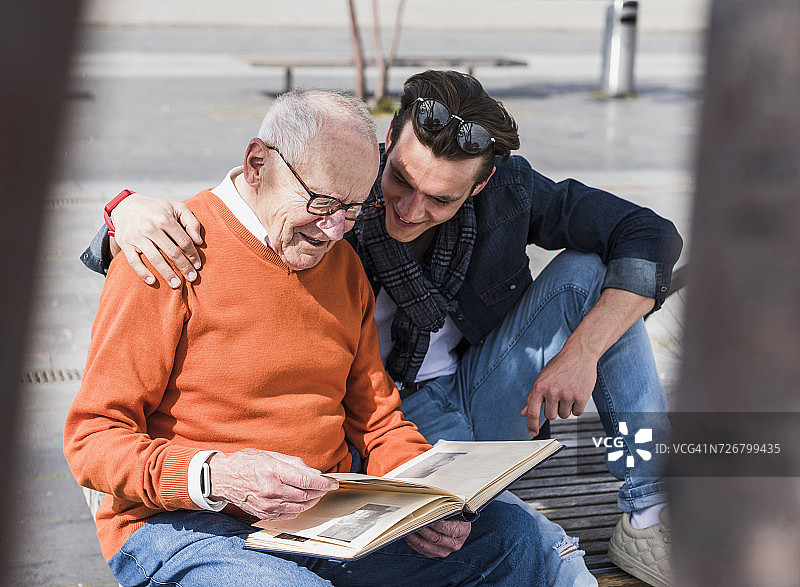 老爷爷和成年的孙子坐在长凳上看相册图片素材