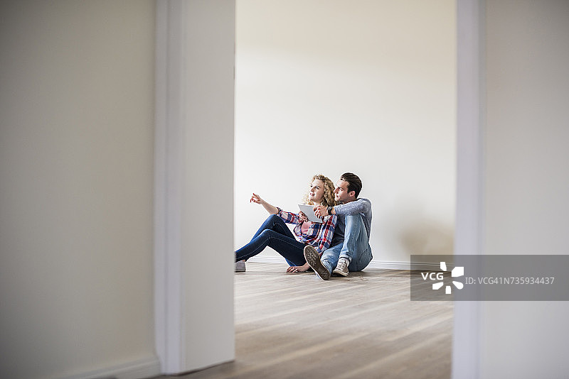 一对年轻夫妇在新家里坐在地板上，手里拿着平板电脑图片素材