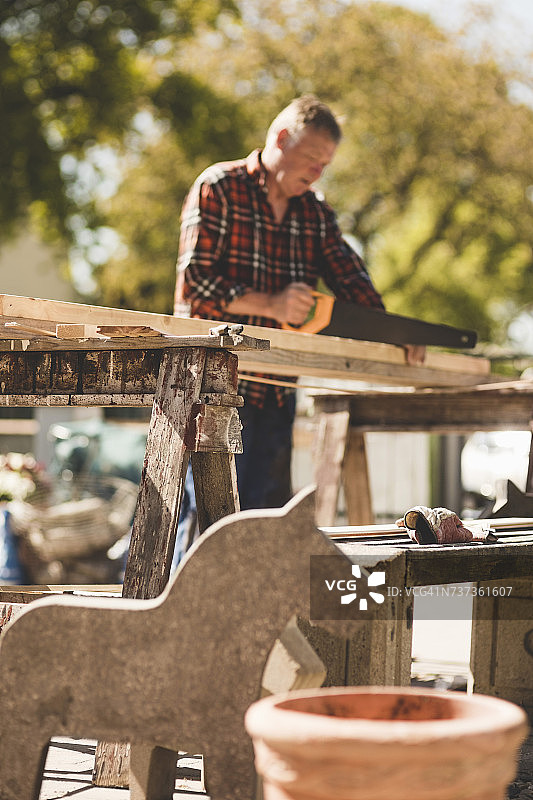 低角度视图的高级男子切割木板与手锯在院子图片素材