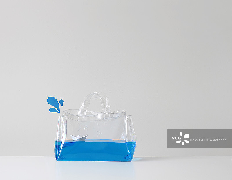 装在透明塑料袋里的纸船漂浮在蓝色的水面上图片素材