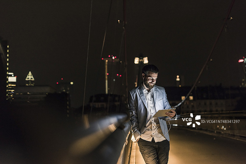 一个年轻人晚上带着平板电脑和耳机在城市大桥上图片素材
