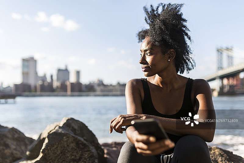 美国，纽约市，布鲁克林，一个女人坐在海边拿着手机图片素材