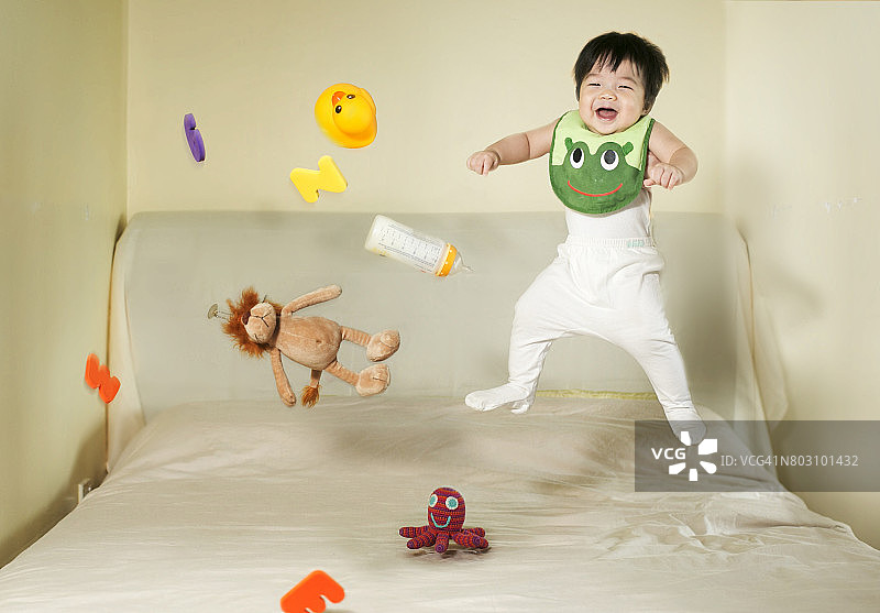 小男孩和玩具在床上跳。图片素材