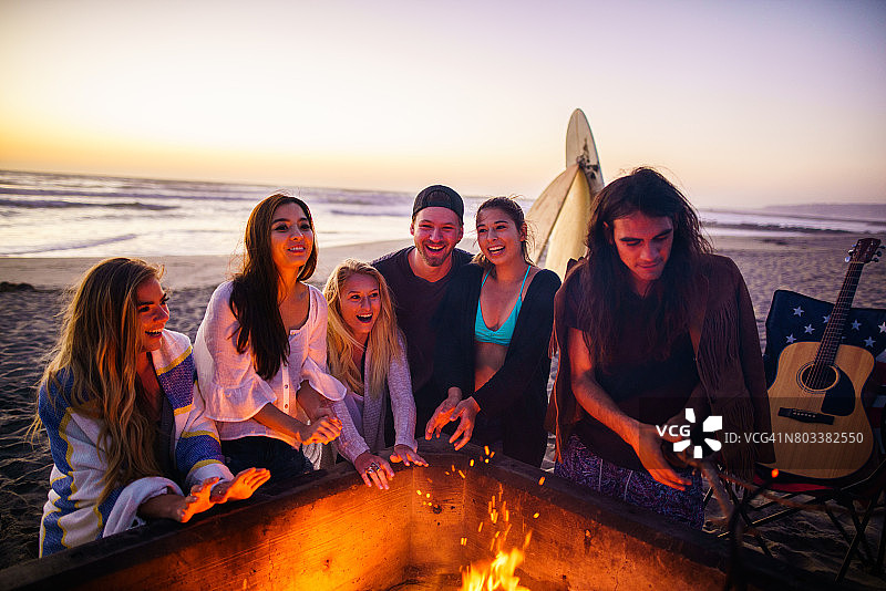 多民族的年轻人，花时间在圣地亚哥的海滩上看日落，弹吉他，在火旁取暖图片素材