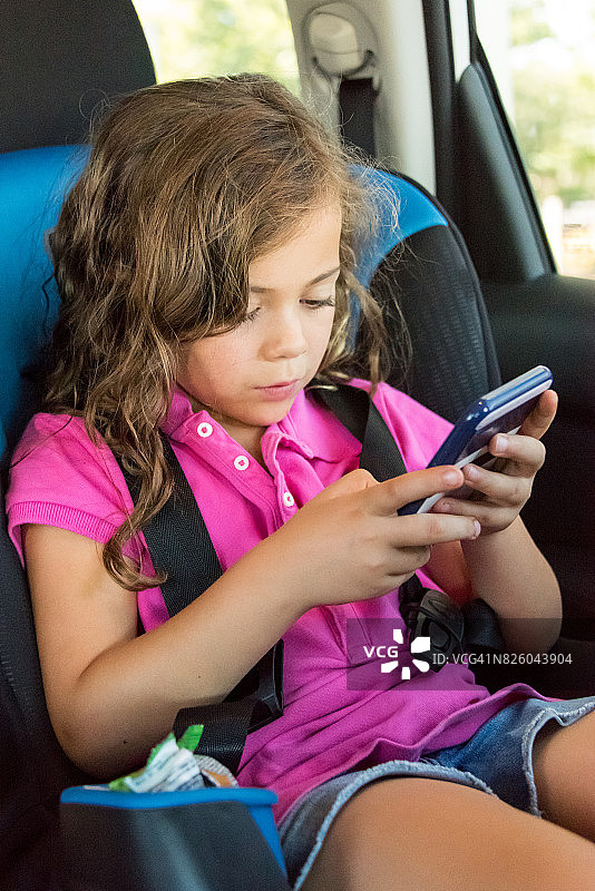 漂亮的小女孩坐在儿童座椅上玩智能手机图片素材