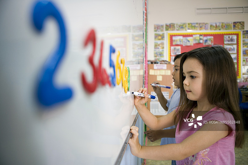 一个小女孩和一个小男孩在教室的白板上写字。图片素材