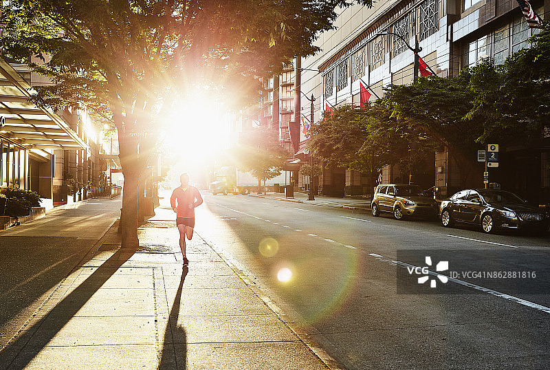 清晨锻炼时，一名男子在空旷的城市街道上跑步图片素材