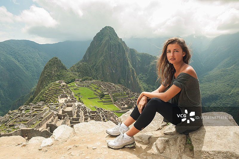 一名年轻女子站在秘鲁古城马丘比丘的悬崖上。图片素材