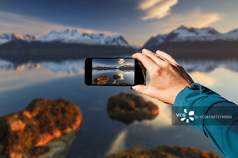 手持智能手机拍照。旅行的概念。挪威，峡湾的日落图片素材