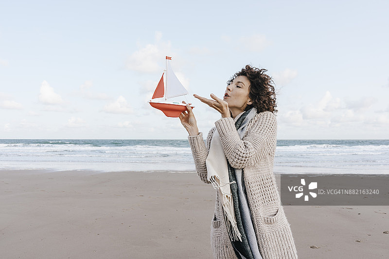 女人对着海滩上的玩具船吹气图片素材
