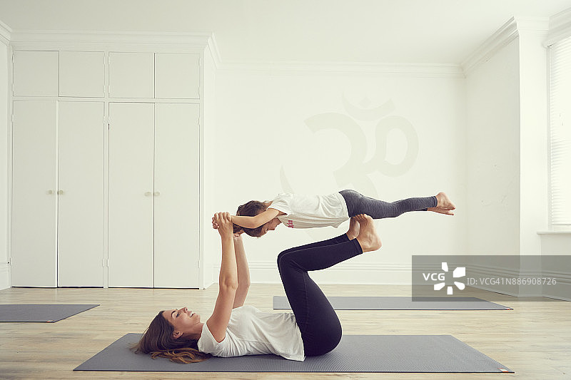 母女在瑜伽房里，女儿在母亲的腿上保持平衡图片素材