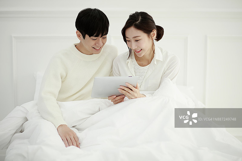 一对年轻夫妇在床上使用平板电脑图片素材