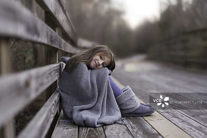 一个棕色长发和棕色眼睛裹在灰色毯子里的年轻女孩图片素材