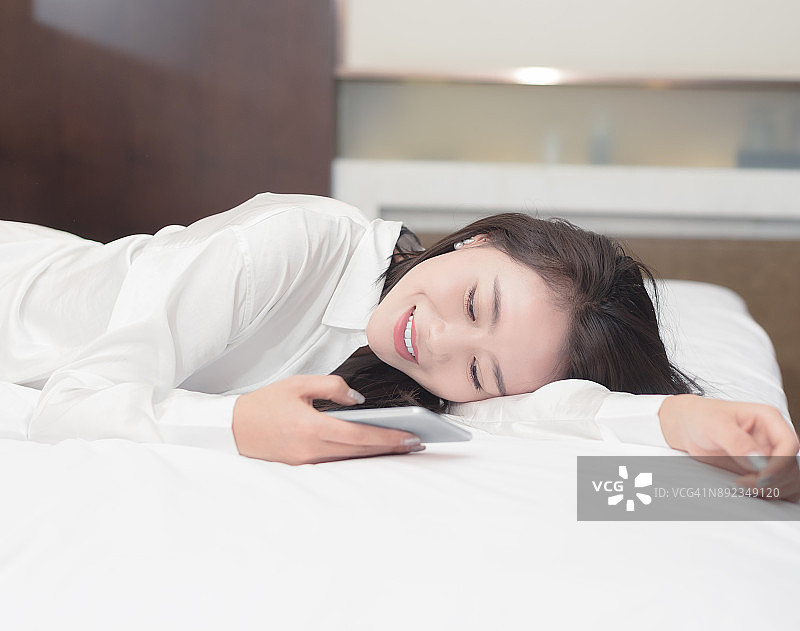 微笑的女人在床上用手机发短信图片素材