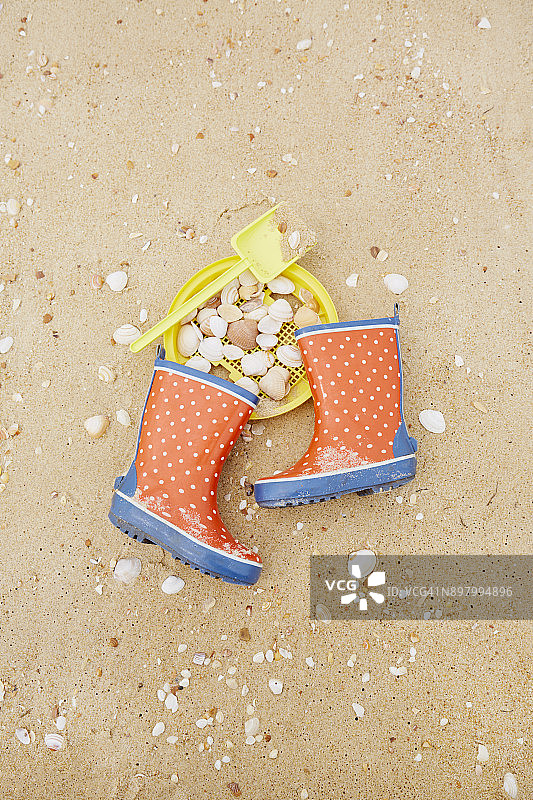 高角度的波点胶靴，铲子，筛子和贝壳在海滩上图片素材