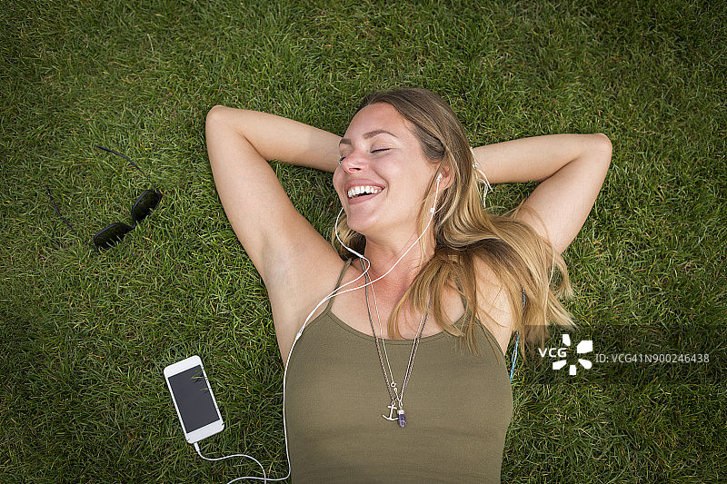 戴着耳机在草坪上休息的快乐年轻女人图片素材