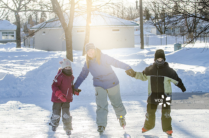 母亲牵着女儿和儿子的手，帮助他们滑冰图片素材
