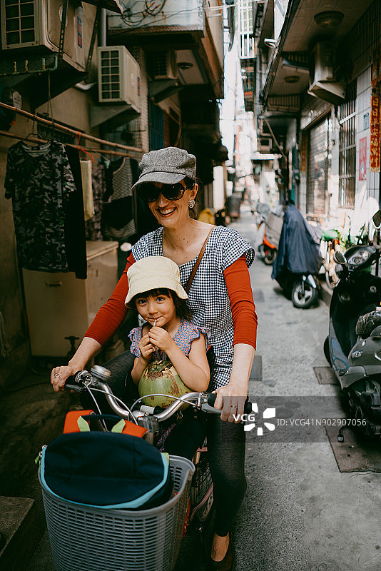 母亲和孩子骑着自行车穿过台湾的后街小巷图片素材