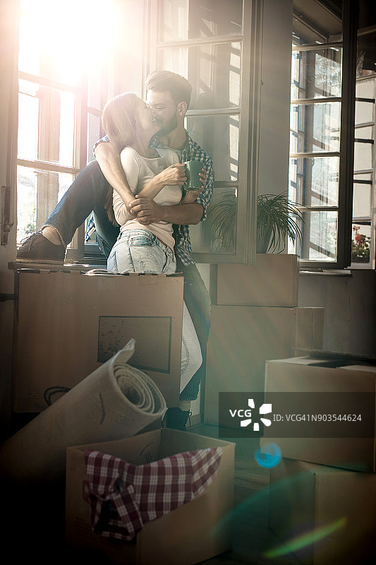 在新家的窗户边，一对年轻的夫妇拥抱着表达爱意。图片素材