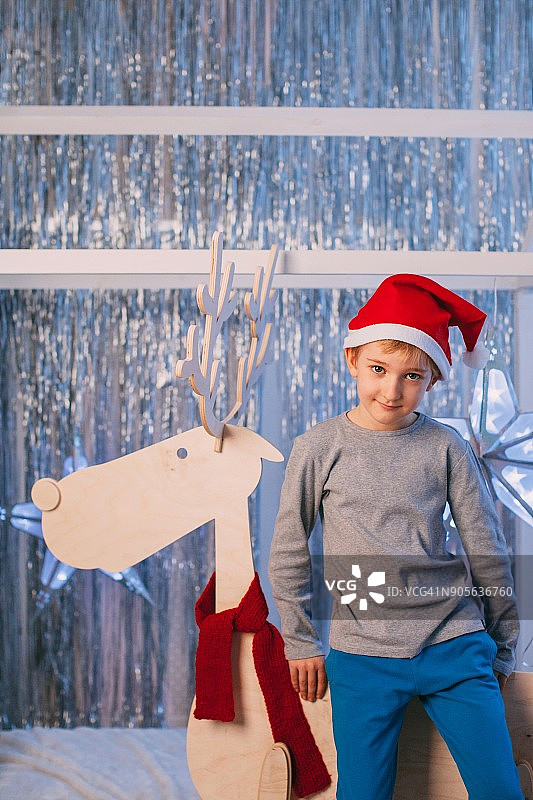 小男孩戴着圣诞帽，坐在玩具驯鹿上图片素材