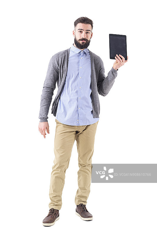 持怀疑态度的年轻大胡子男子拿着并展示平板电脑。图片素材