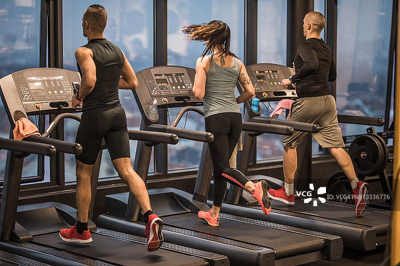 运动员在健身房跑步机上慢跑的后视图。图片素材