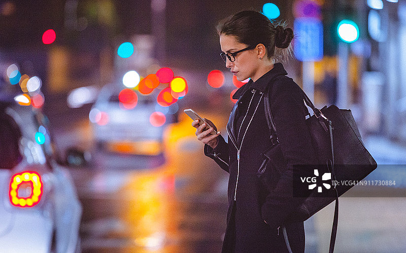 年轻女子晚上在城市街道上使用智能手机图片素材
