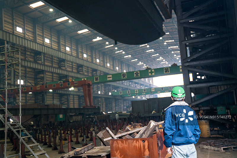 在大型工厂中，监督用起重机吊起大型船舶部件的领班图片素材