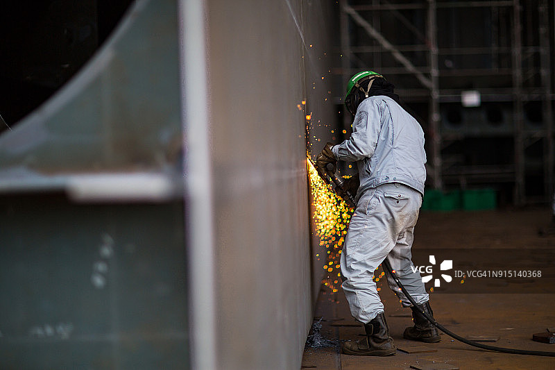 一名钢铁工人正在打磨大型轮船零件，火花四溅图片素材