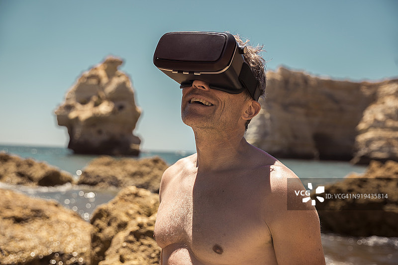 成熟的男人戴着VR眼镜在海滩的岩石之间图片素材