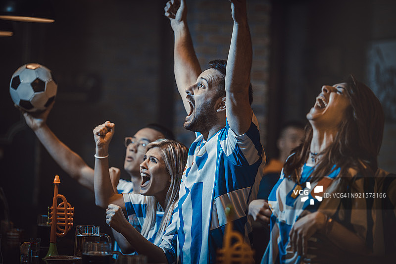 酒吧里一群兴奋的足球迷在电视上观看一场成功的比赛。图片素材