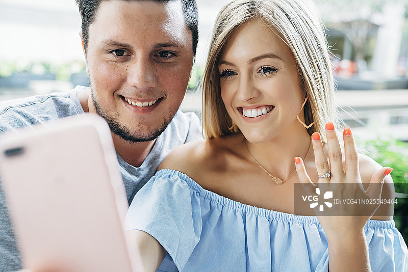 一对白人夫妇摆姿势用手机自拍展示订婚戒指图片素材