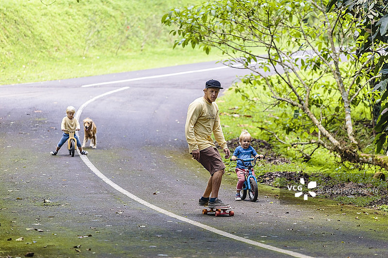 骑滑板的父亲陪着骑自行车的儿子们图片素材