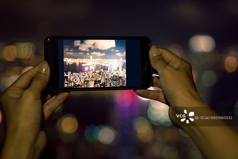 手持手机智能手机以散景光为背景拍照，智能手机以城市景为屏幕，模糊城市散景图片素材