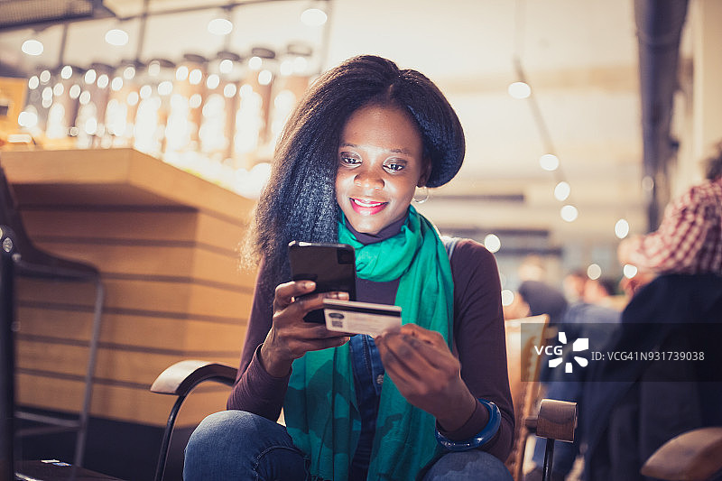 一个年轻的非洲裔美国女人，在网上，用信用卡购物，在咖啡店的休息时间喝咖啡图片素材