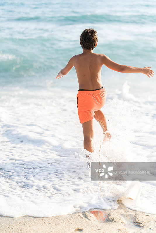 年轻的男孩在海滩上跑在水里图片素材