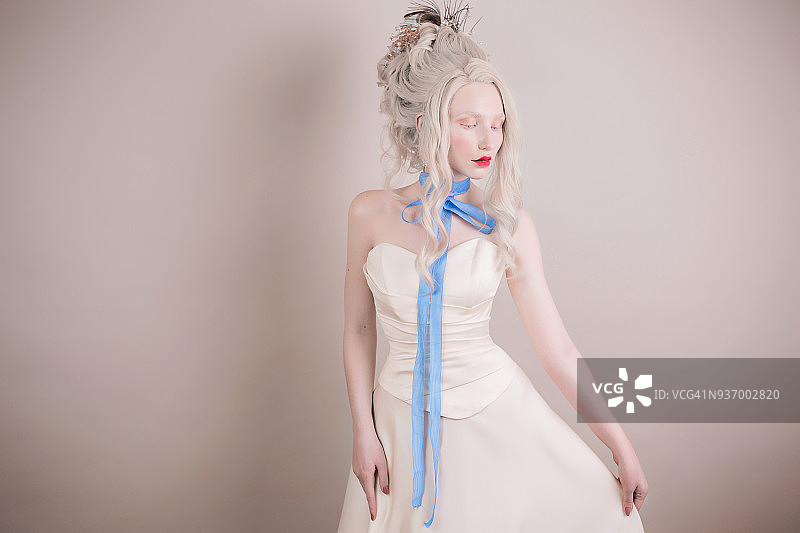 一个金发女人，有着美丽奢华的洛可可式发型，穿着白色的裙子，灰色的背景下脖子上系着蓝色的缎带。图片素材