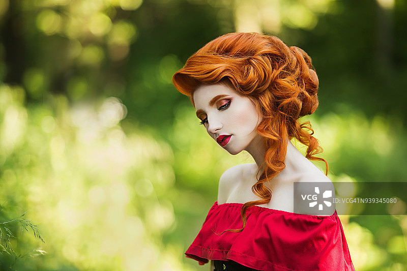 美丽的红发女孩在绿色的背景下摆姿势。夏日森林里一个红头发女人的肖像图片素材