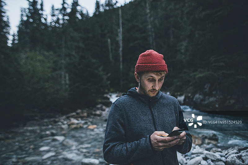 加拿大，不列颠哥伦比亚省，冰川国家公园，一名男子在森林里的Illecillewaet河上拿着手机图片素材