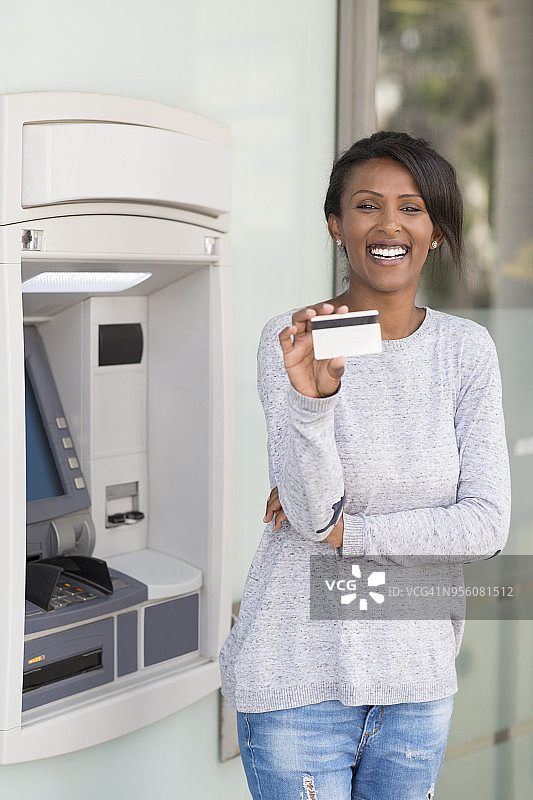 满意的银行客户女士出示信用卡/借记卡。图片素材