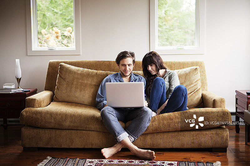 一个男人和女朋友坐在家里的沙发上玩笔记本电脑图片素材