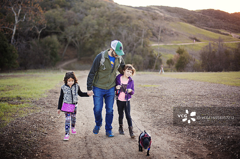 父亲和女儿带着狗走在山路上图片素材
