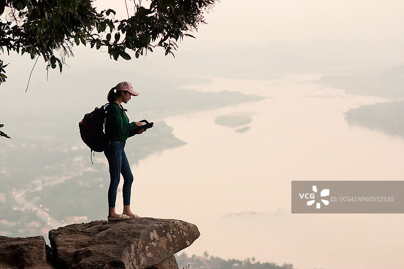 快乐的旅行者女人拿着一个背包站在山顶向下看图片素材