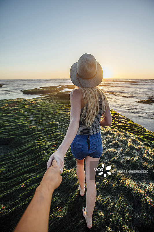 日落时分，一个男人牵着女朋友的手在海滩的草地上散步图片素材